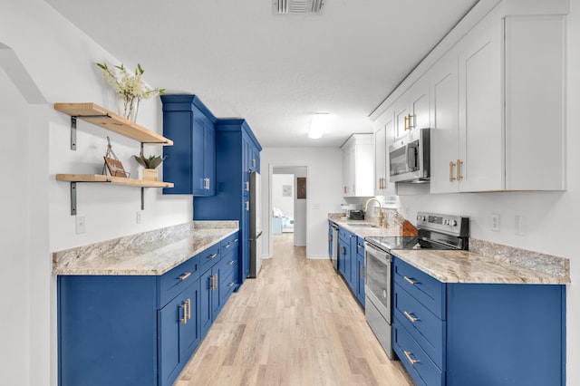 kitchen with light hardwood / wood-style flooring, blue cabinets, white cabinetry, appliances with stainless steel finishes, and a textured ceiling