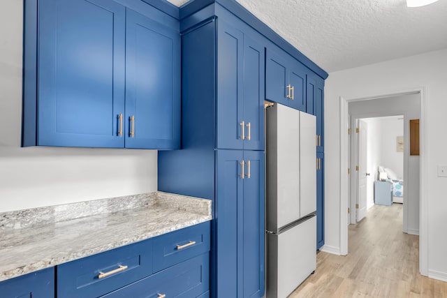 kitchen with light hardwood / wood-style floors, blue cabinetry, white refrigerator, and light stone counters