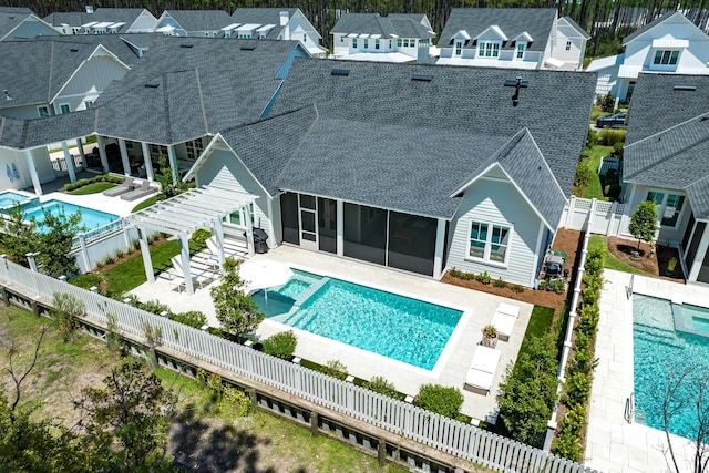 rear view of house featuring a sunroom, a fenced backyard, a residential view, roof with shingles, and a pool with connected hot tub