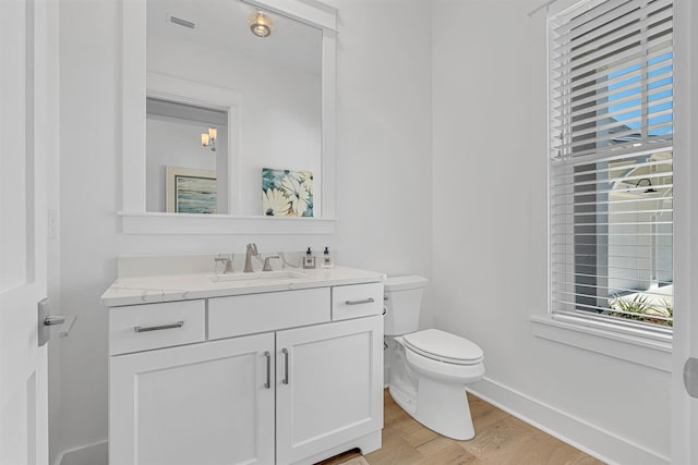 half bath featuring toilet, baseboards, wood finished floors, and vanity