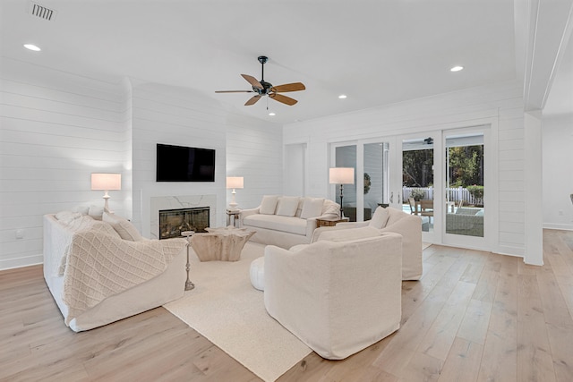 living room with ceiling fan, a fireplace, wood walls, and light hardwood / wood-style flooring