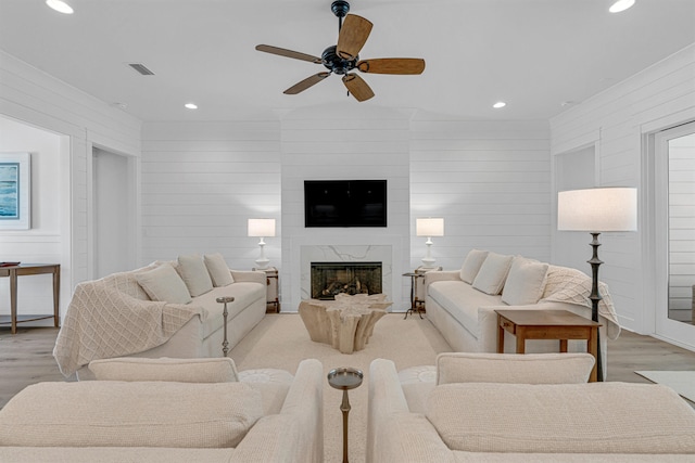 living room featuring wood walls, ceiling fan, light hardwood / wood-style floors, and a premium fireplace