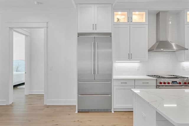 kitchen with wall chimney exhaust hood, white cabinets, light hardwood / wood-style flooring, and premium appliances