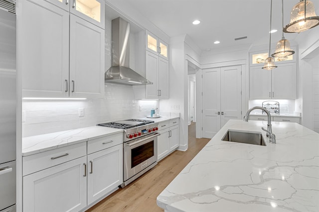 kitchen with light hardwood / wood-style flooring, sink, pendant lighting, wall chimney range hood, and premium appliances