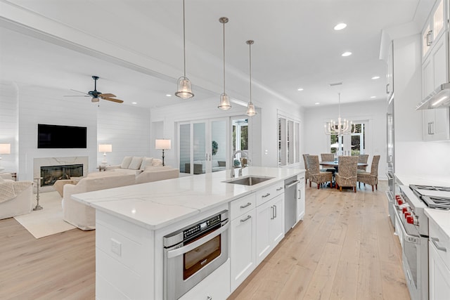 kitchen with sink, appliances with stainless steel finishes, an island with sink, light hardwood / wood-style floors, and ceiling fan with notable chandelier