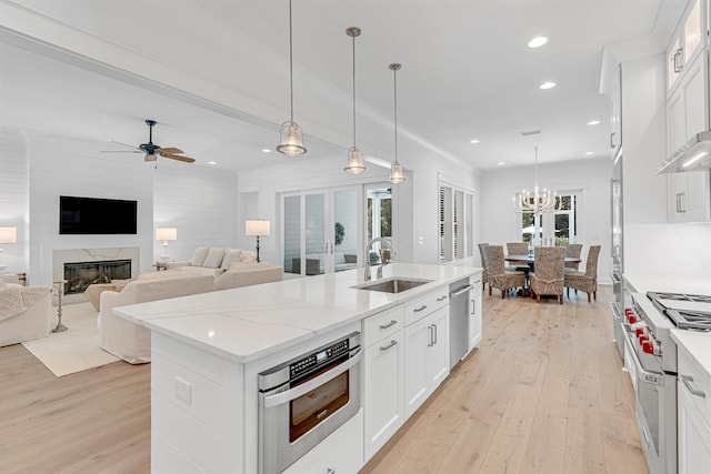 kitchen featuring pendant lighting, stainless steel appliances, white cabinets, a kitchen island with sink, and a sink