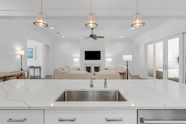 kitchen with sink, white cabinets, a large fireplace, and light stone countertops