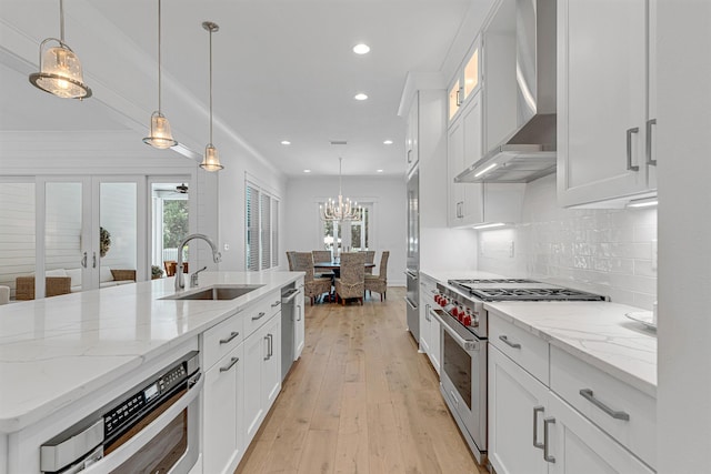 kitchen with white cabinets, wall chimney exhaust hood, appliances with stainless steel finishes, decorative light fixtures, and a sink