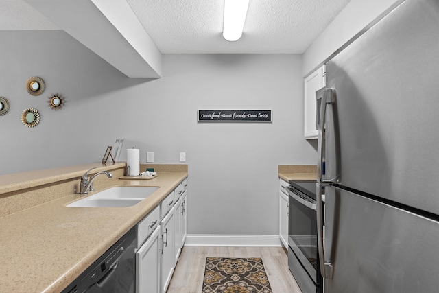 kitchen featuring appliances with stainless steel finishes, white cabinetry, sink, light wood-type flooring, and a textured ceiling