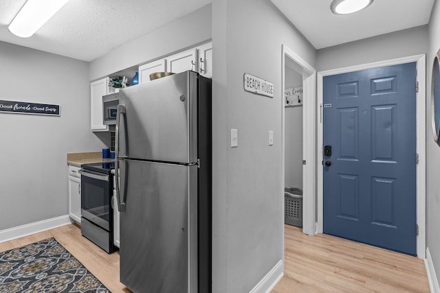 kitchen featuring a textured ceiling, stainless steel appliances, white cabinetry, and light wood-type flooring