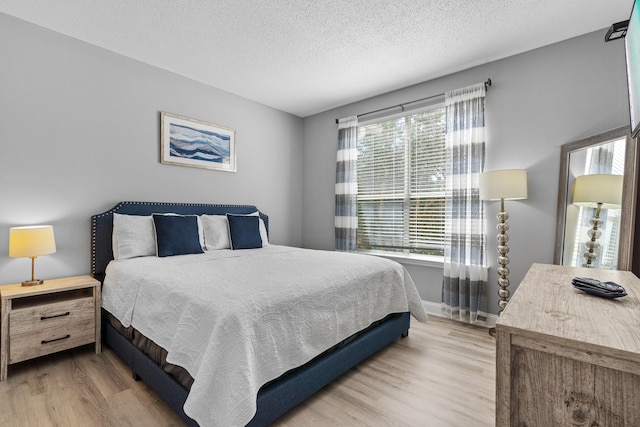 bedroom with a textured ceiling, light hardwood / wood-style floors, and multiple windows