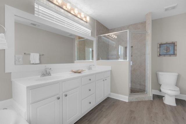 bathroom with double vanity, visible vents, wood finished floors, a shower stall, and a sink