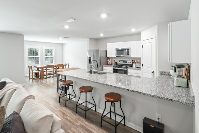 kitchen with appliances with stainless steel finishes, light hardwood / wood-style flooring, sink, light stone countertops, and white cabinets