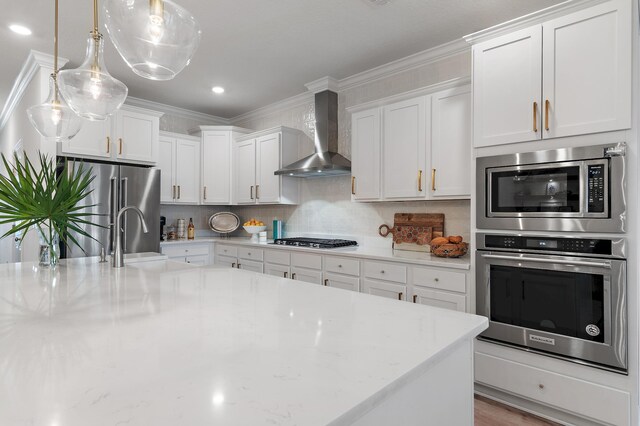 kitchen featuring decorative light fixtures, appliances with stainless steel finishes, decorative backsplash, wall chimney range hood, and white cabinets