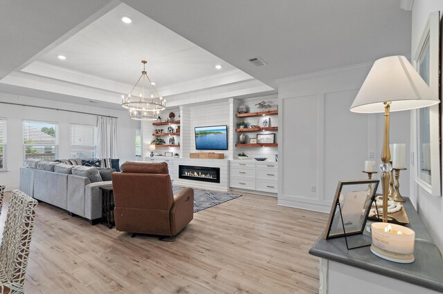 living room featuring built in shelves, a raised ceiling, light hardwood / wood-style flooring, an inviting chandelier, and crown molding