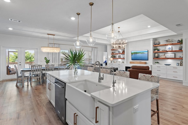 kitchen with light wood-type flooring, a kitchen island with sink, pendant lighting, and a tray ceiling