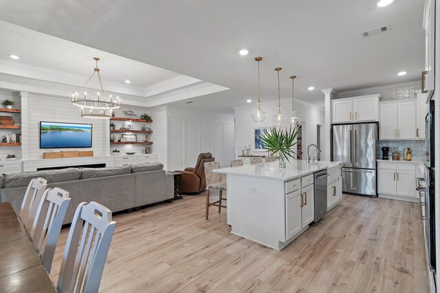 kitchen with appliances with stainless steel finishes, light hardwood / wood-style flooring, white cabinetry, a kitchen island with sink, and hanging light fixtures