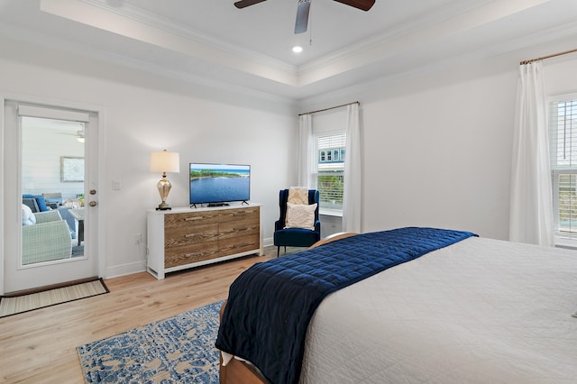 bedroom with light wood-type flooring, a raised ceiling, and multiple windows