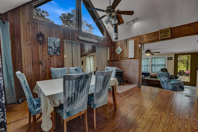 dining room featuring ceiling fan, high vaulted ceiling, wood-type flooring, and wooden walls