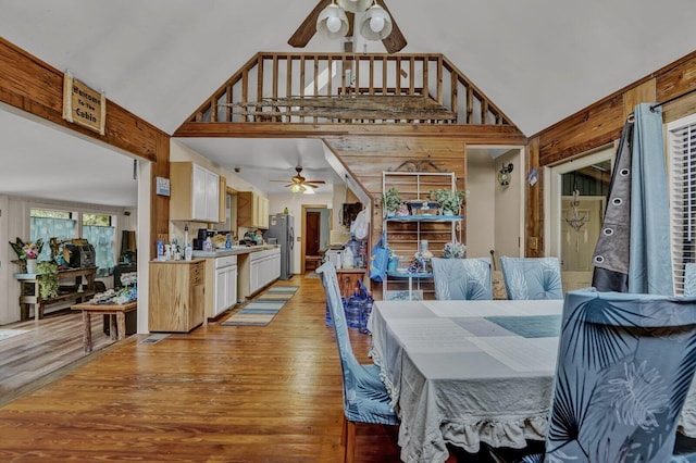 dining area with wood walls, light hardwood / wood-style flooring, ceiling fan, and high vaulted ceiling