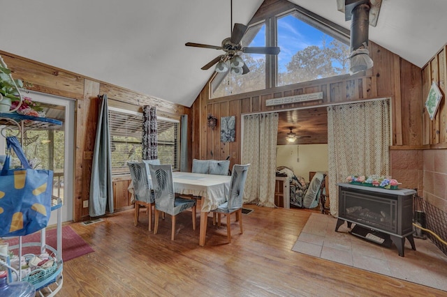 dining space featuring wood walls, ceiling fan, hardwood / wood-style floors, and a wood stove