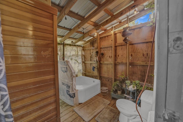 bathroom featuring independent shower and bath, toilet, wooden walls, hardwood / wood-style floors, and beam ceiling