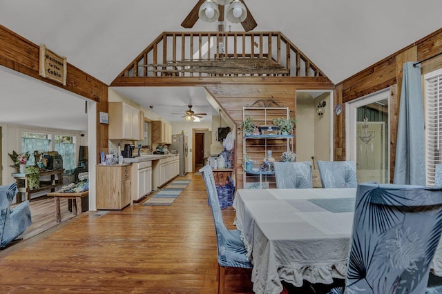 dining area featuring ceiling fan, a towering ceiling, light hardwood / wood-style floors, and wooden walls