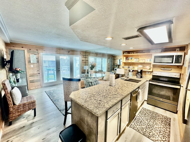 kitchen featuring light stone counters, stainless steel appliances, a sink, open floor plan, and light wood finished floors