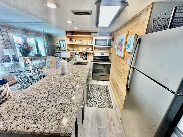 kitchen featuring wooden walls, a sink, visible vents, appliances with stainless steel finishes, and light stone countertops