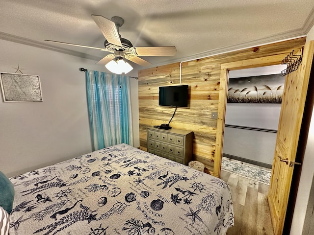 bedroom with ceiling fan, wood finished floors, crown molding, a textured ceiling, and wood walls