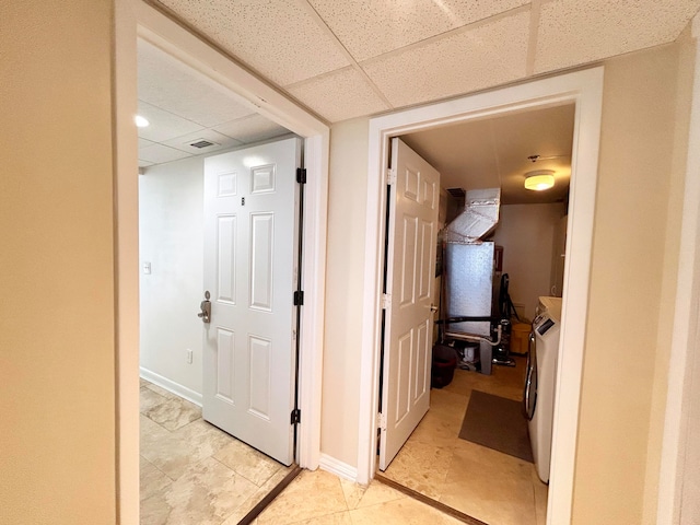 hallway featuring a drop ceiling, light tile patterned floors, and independent washer and dryer