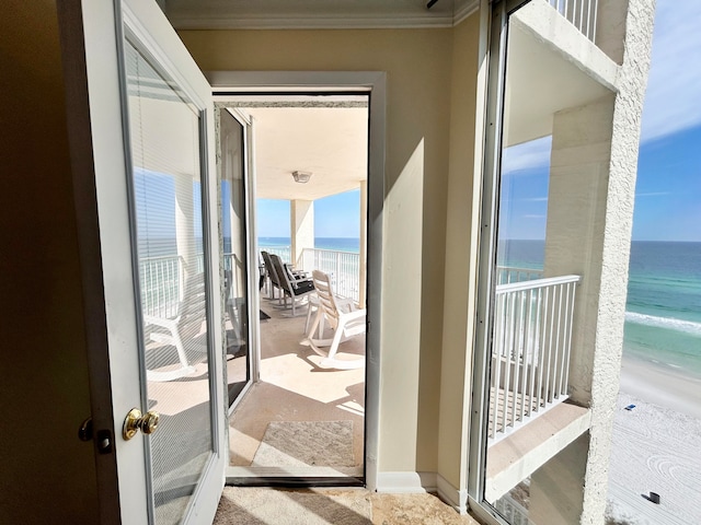 entryway featuring a beach view, a water view, and crown molding