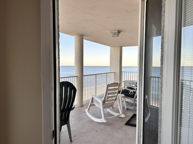 balcony at dusk featuring a water view and a beach view