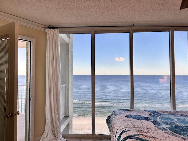 bedroom with a view of the beach, a textured ceiling, a water view, and multiple windows