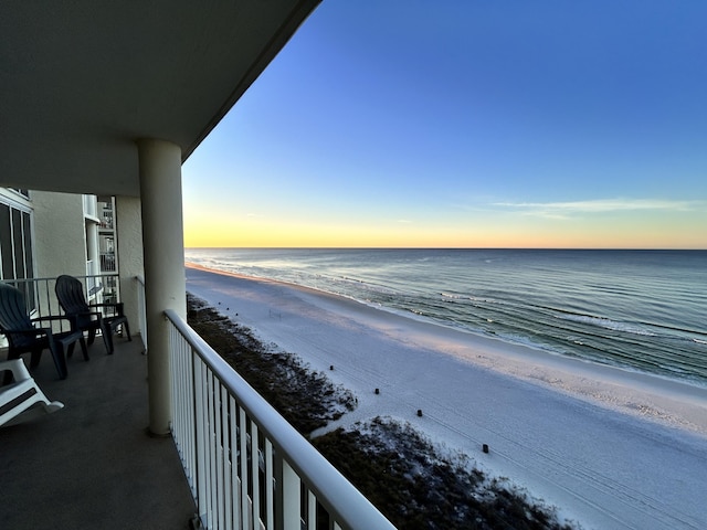 balcony at dusk featuring a beach view and a water view