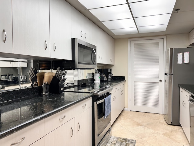 kitchen with a paneled ceiling, white cabinetry, dark stone counters, and appliances with stainless steel finishes