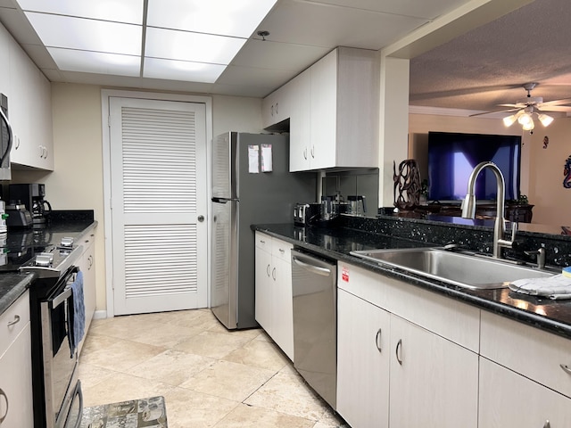 kitchen with appliances with stainless steel finishes, ceiling fan, sink, dark stone countertops, and white cabinets