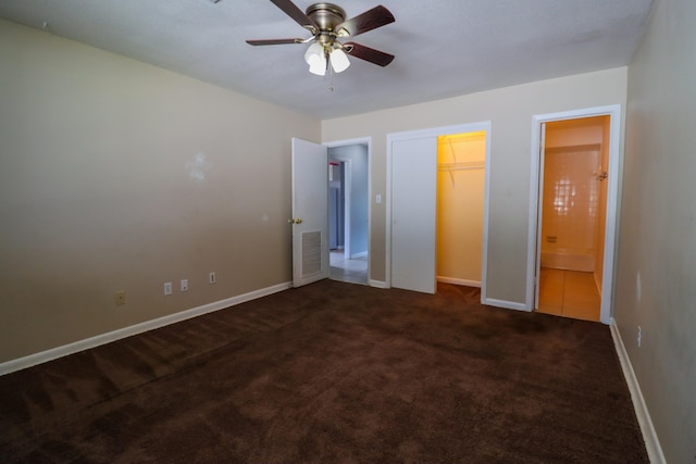 unfurnished bedroom with ceiling fan, dark carpet, and ensuite bathroom