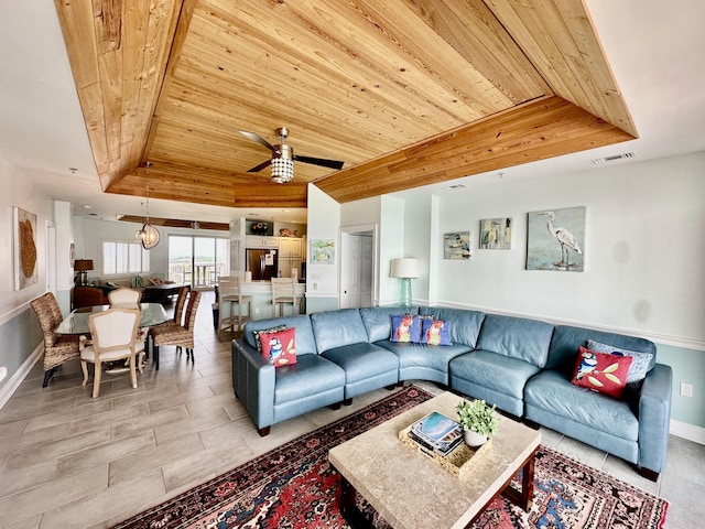 living room with a tray ceiling, visible vents, ceiling fan, wooden ceiling, and baseboards