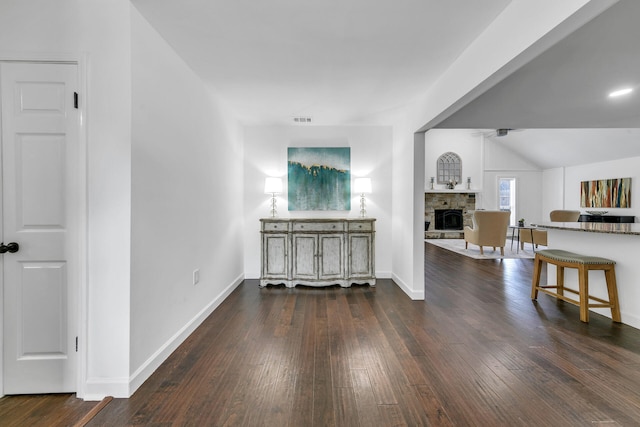 interior space featuring visible vents, dark wood-type flooring, vaulted ceiling, a stone fireplace, and baseboards