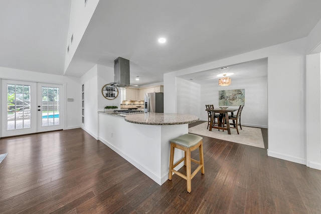 kitchen featuring a breakfast bar, french doors, island exhaust hood, stainless steel appliances, and a peninsula