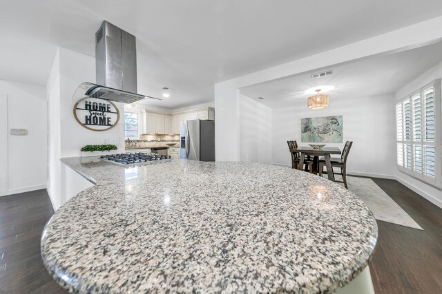 kitchen with dark hardwood / wood-style floors, backsplash, cream cabinets, light stone countertops, and stainless steel appliances