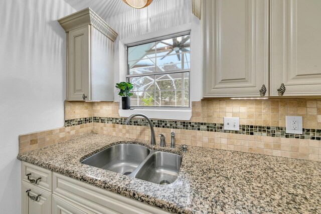 kitchen with white cabinetry, backsplash, sink, and light stone countertops