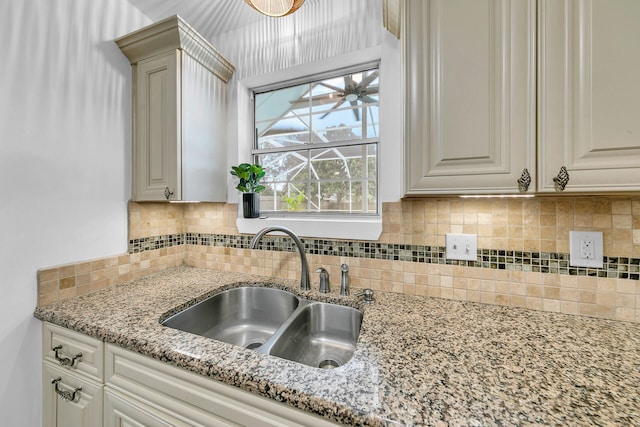 kitchen featuring white cabinets, light stone countertops, decorative backsplash, and a sink