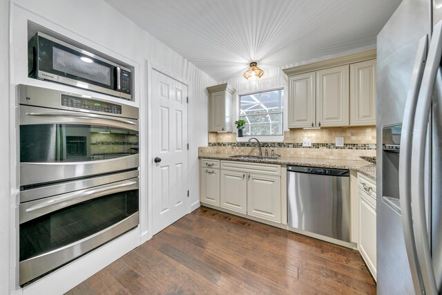 kitchen featuring appliances with stainless steel finishes, a sink, dark wood-style floors, and light stone countertops