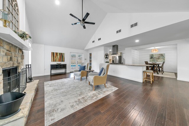 living room featuring hardwood / wood-style flooring, high vaulted ceiling, ceiling fan, and a stone fireplace