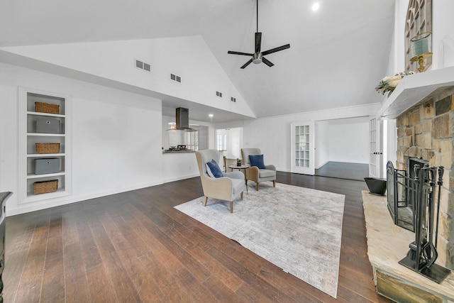 living area with ceiling fan, a stone fireplace, built in shelves, visible vents, and dark wood finished floors