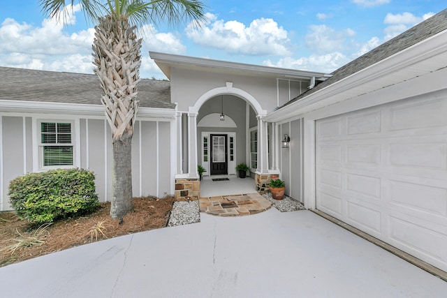 doorway to property featuring an attached garage, roof with shingles, and stucco siding