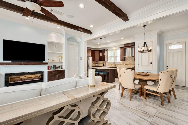 tiled dining room featuring sink, ornamental molding, built in features, beam ceiling, and ceiling fan with notable chandelier