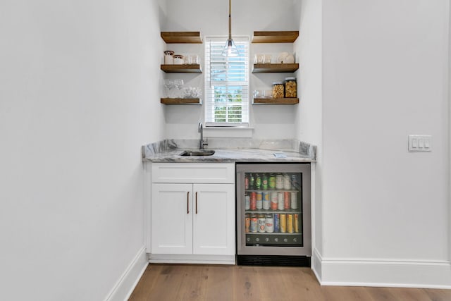 bar with sink, light hardwood / wood-style floors, beverage cooler, pendant lighting, and white cabinets